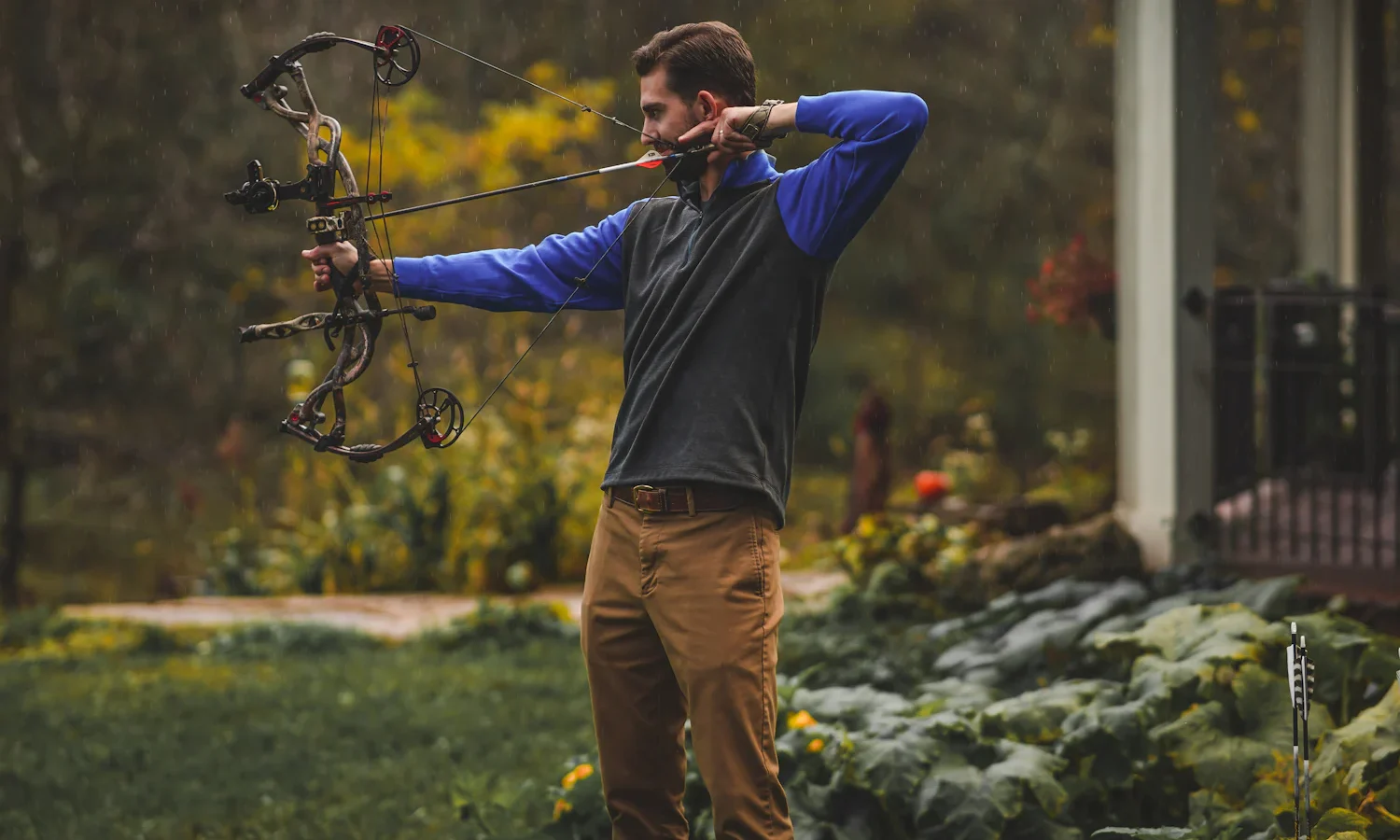 Archer at full draw with a compound bow in a garden
