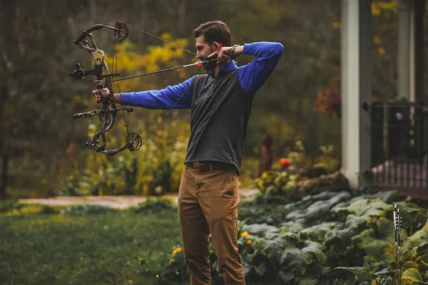 Archer at full draw with a compound bow in a garden
