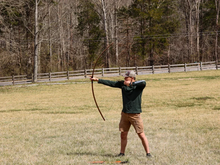 Archer at full draw with a longbow in an open field