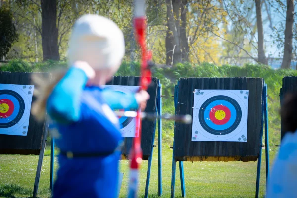 Archer in a blue jacket holding a recurve bow in front of target faces, seen from behind