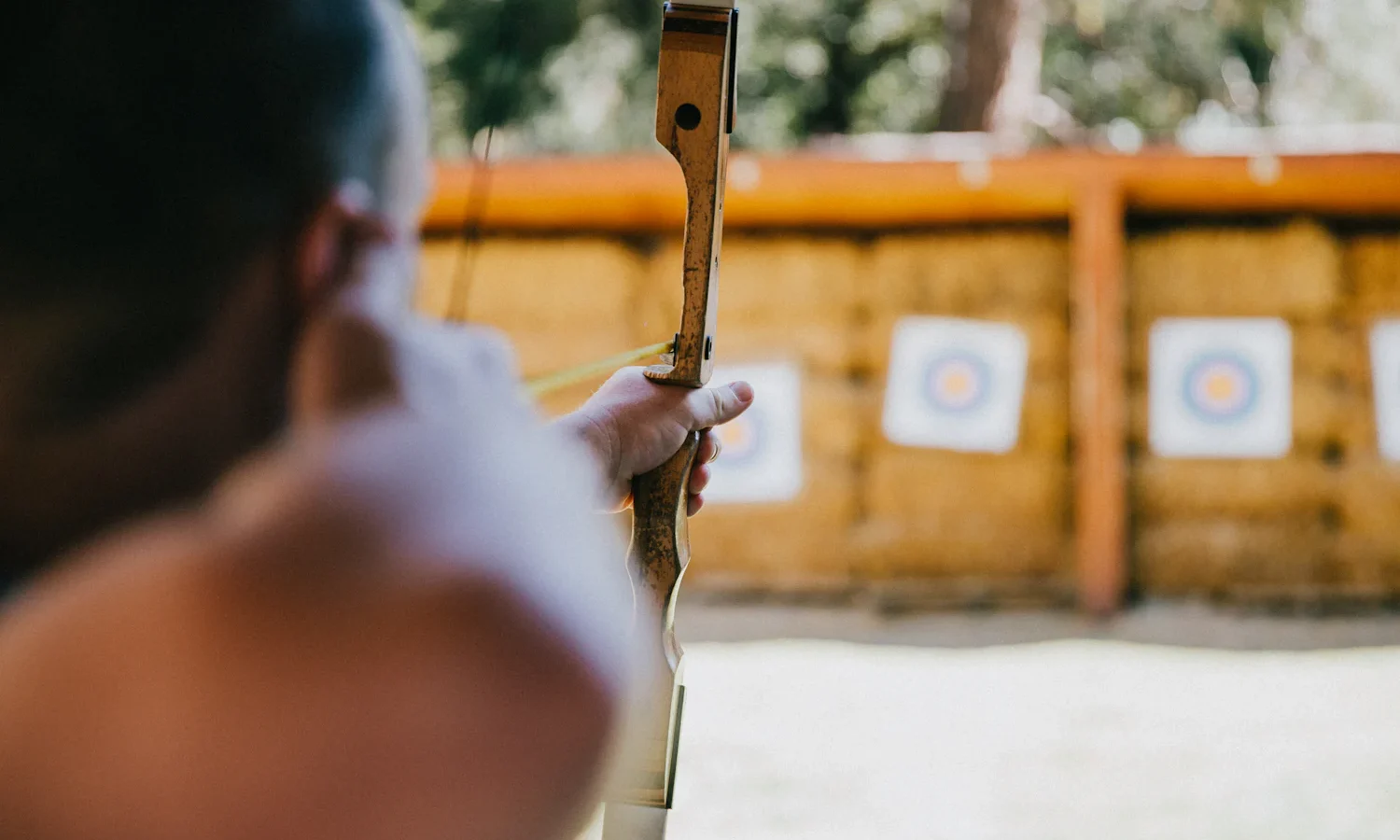 Archer seen from behind raising a wooden bow toward target faces on straw bales