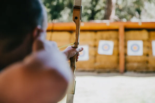 Archer seen from behind raising a wooden bow toward target faces on straw bales