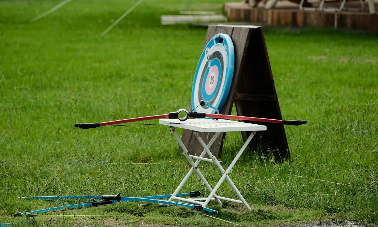 Archery target on a stand with a recurve bow resting on a folding table on a lawn