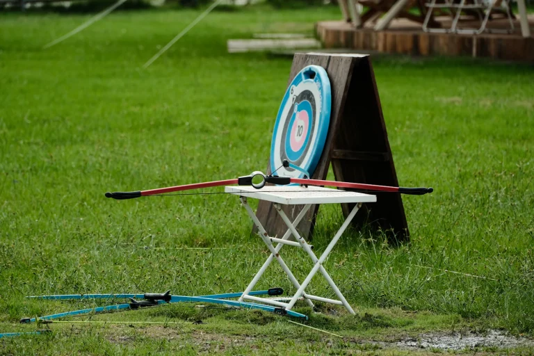 Archery target on a stand with a recurve bow resting on a folding table on a lawn