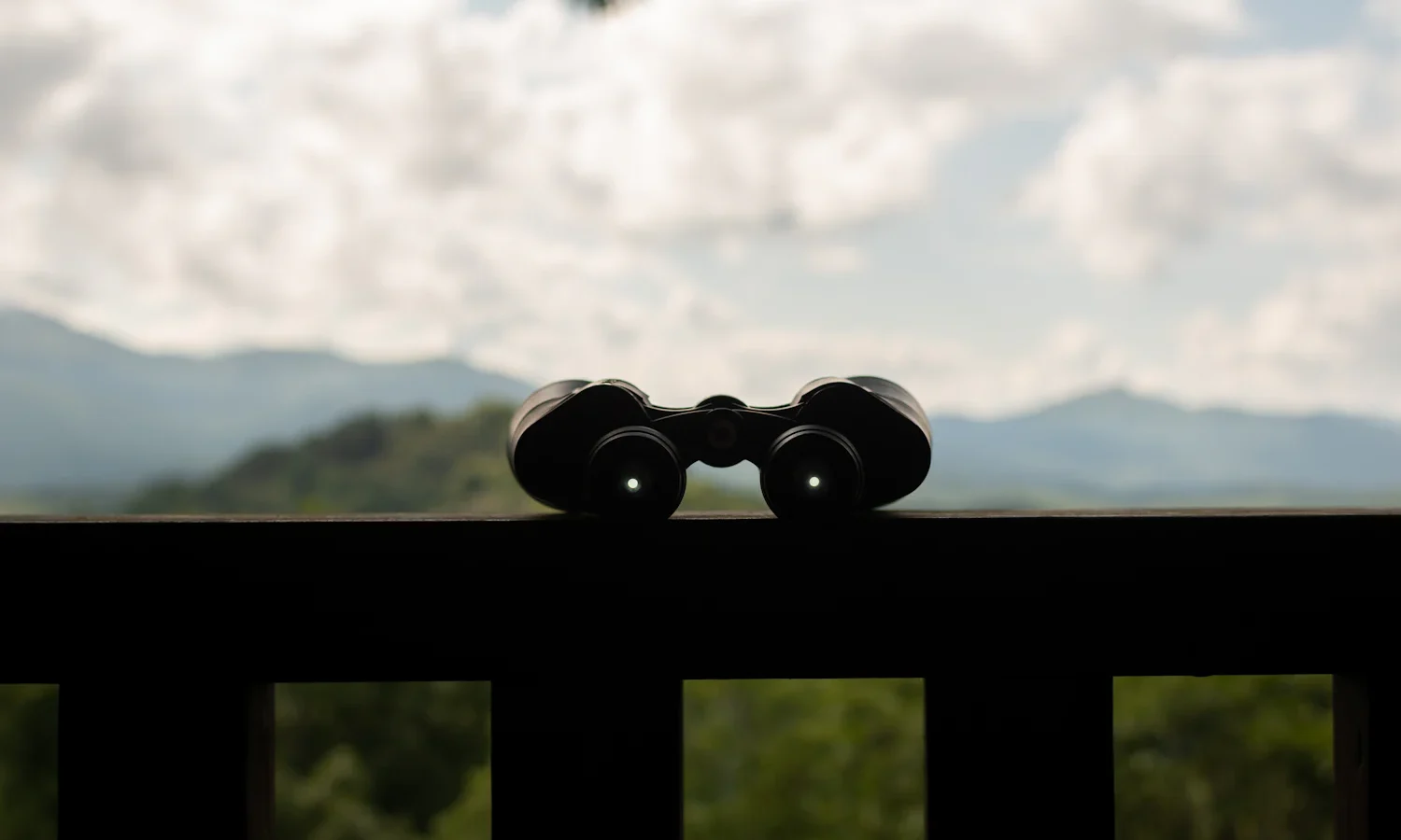 Binoculars resting on a railing with hills in the distance