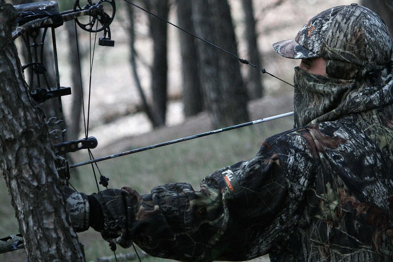 Bowhunter in full camouflage and face mask at full draw with a compound bow