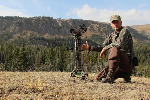 Bowhunter kneeling with a compound bow in a mountain meadow