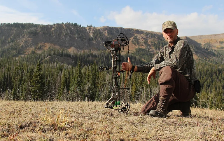 Bowhunter kneeling with a compound bow in a mountain meadow