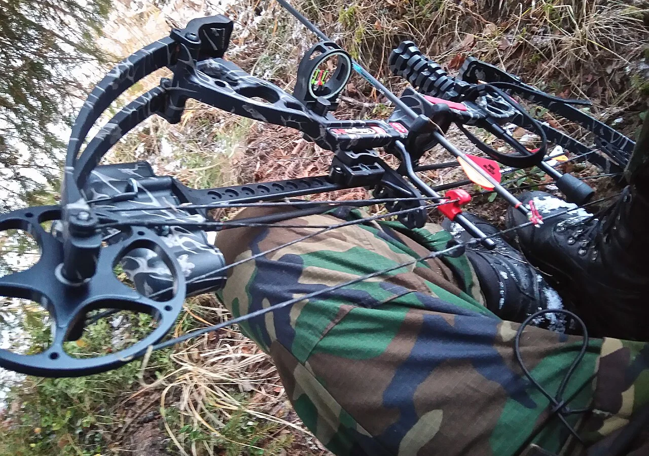 Close-up of a compound bow's cams, cables and arrow resting across a hunter's camouflage clothing