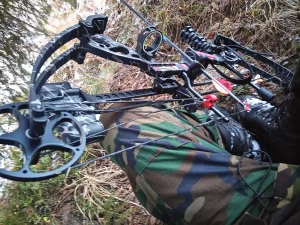 Close-up of a compound bow's cams, cables and arrow resting across a hunter's camouflage clothing