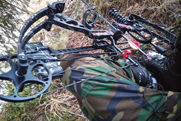 Close-up of a compound bow's cams, cables and arrow resting across a hunter's camouflage clothing