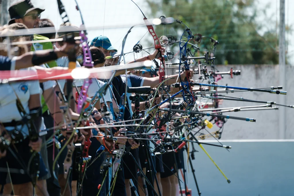 Line of compound bows with long stabilizers held at full draw on a competition shooting line