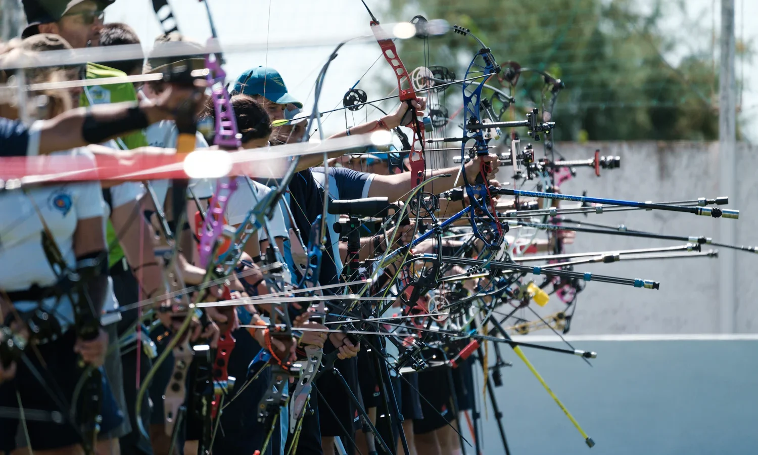 Line of compound bows with long stabilizers held at full draw on a competition shooting line