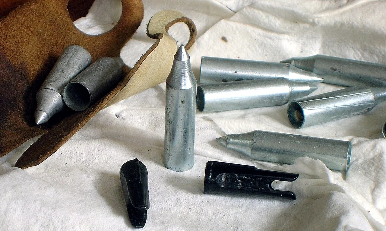 Arrow field points and plastic nocks laid out beside a leather finger tab