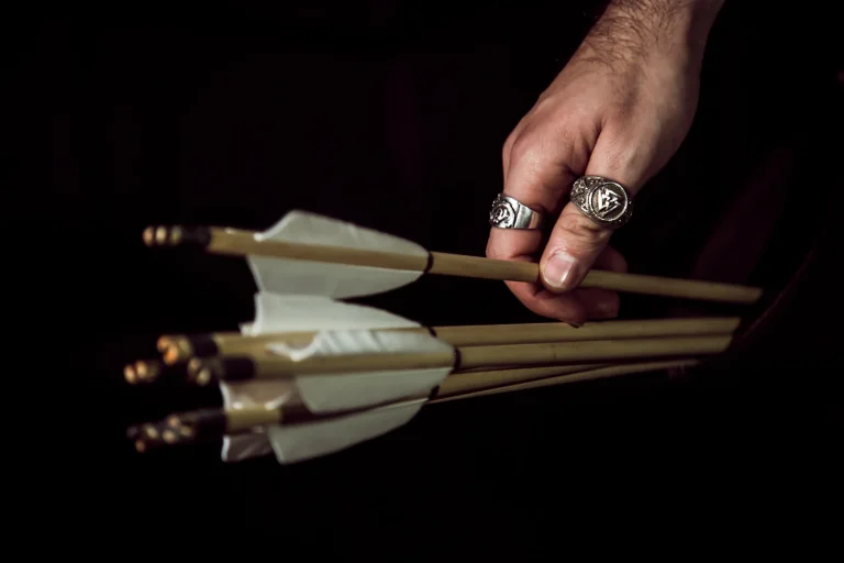 Hand holding arrows with white feather fletching against a dark background