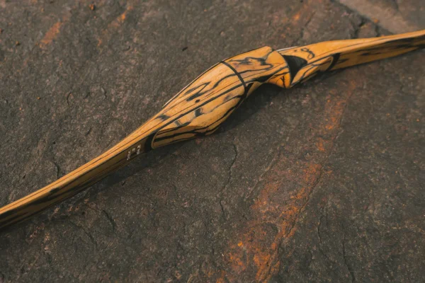 Laminated wooden recurve bow lying on a dark stone surface