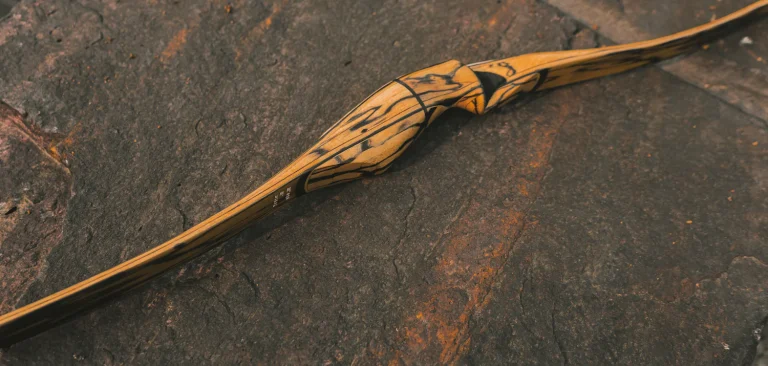 Laminated wooden recurve bow lying on a dark stone surface