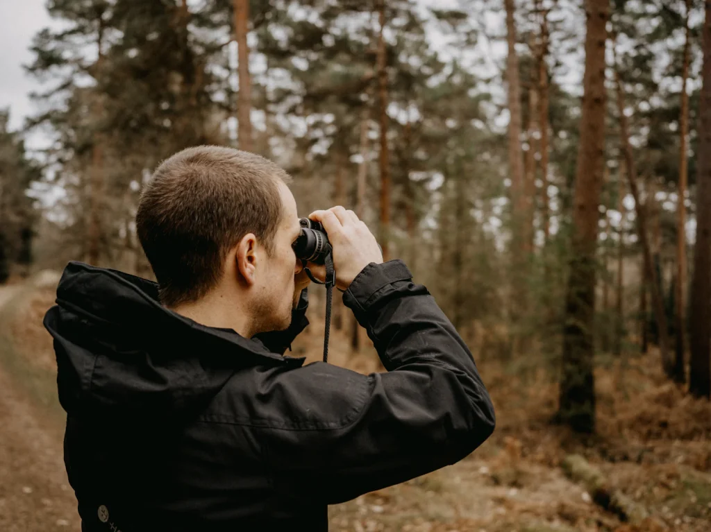 Man in a pine forest looking through binoculars