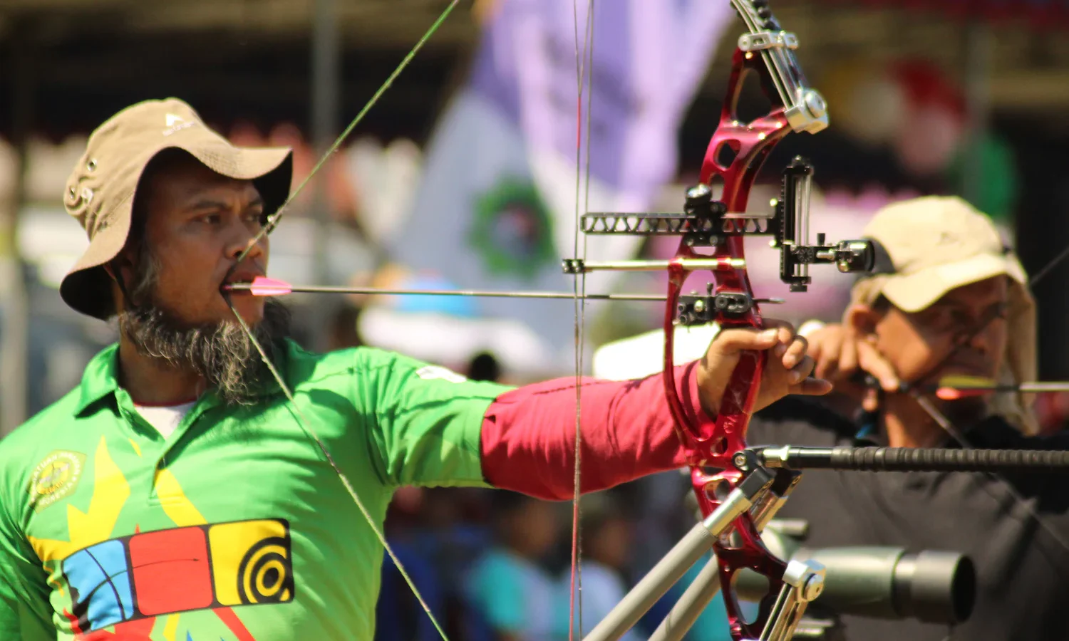 Competitor aiming a target compound bow fitted with a scope sight and a long stabilizer