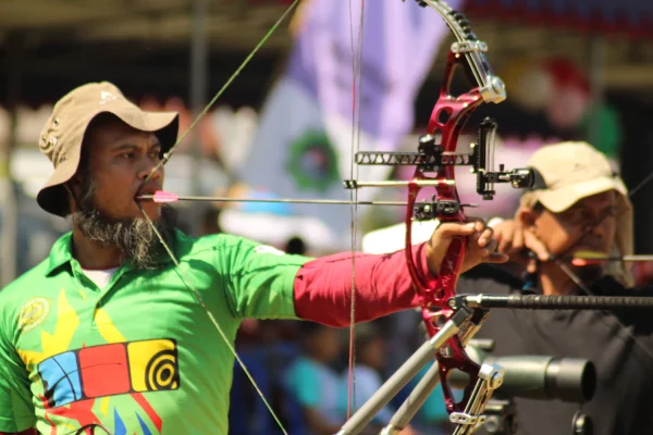 Competitor aiming a target compound bow fitted with a scope sight and a long stabilizer