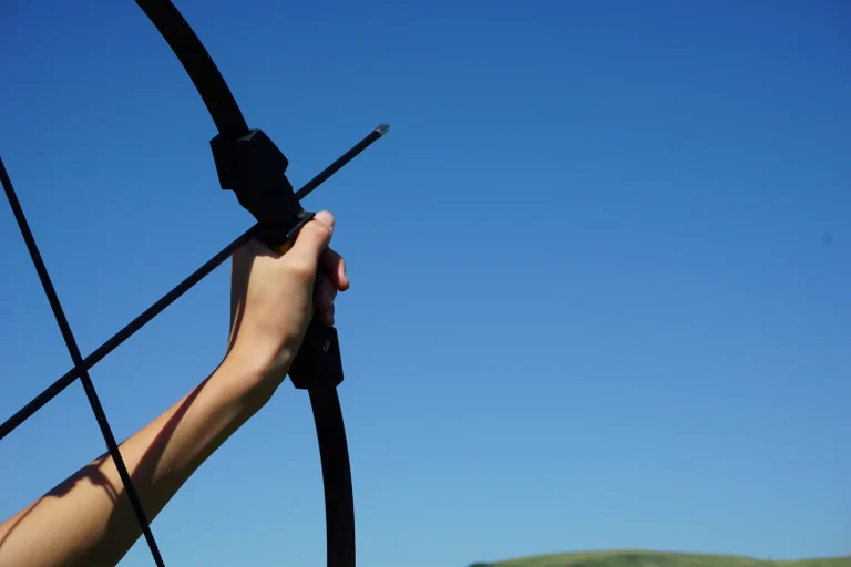 Hand holding a traditional bow with an arrow on the string against a clear blue sky