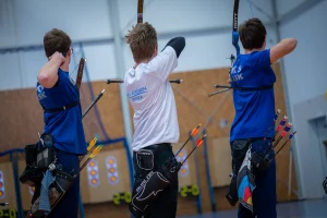 Three young archers shooting at an indoor range, seen from behind
