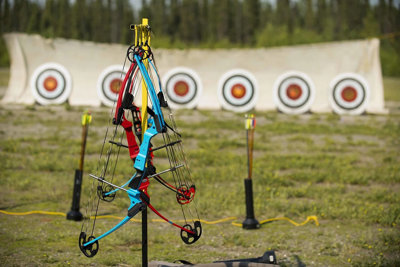 Youth compound bows hanging on a rack in front of a row of target faces
